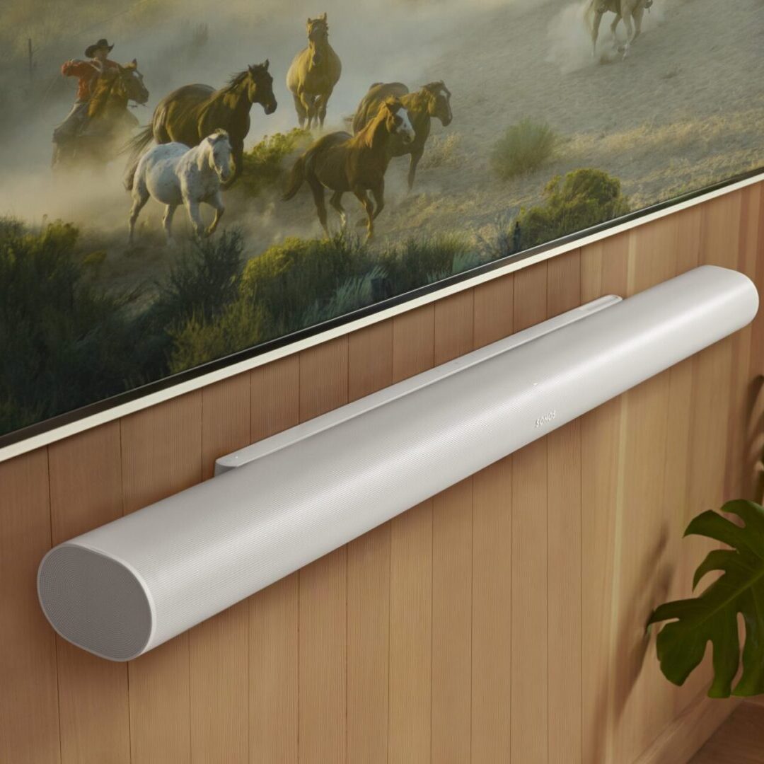 A sleek Sonos Arc soundbar mounted neatly below a wall-mounted TV, showcasing its slim, modern design and premium matte finish. The soundbar features subtle branding, a gently curved profile, and discrete speaker grilles, emphasizing its elegant look and seamless integration into contemporary living spaces.